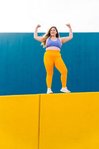 Full length of woman jumping against yellow wall