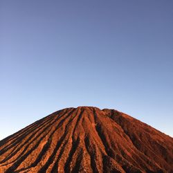 Low angle view of volcanic mountain against clear blue sky