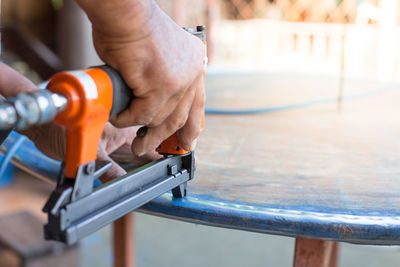 Cropped hand of carpenter holding work tool on table in workshop