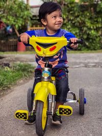 Smiling boy riding tricycle on road