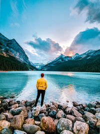 Rear view of man standing on rock by lake against sky