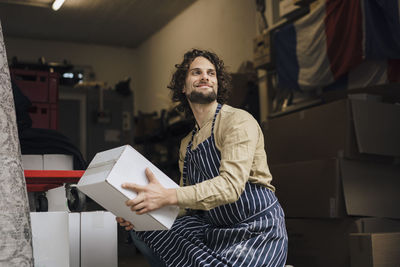 Smiling young businessman carrying cardboard box in storage room