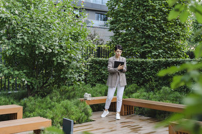 Businesswoman using tablet pc standing by bench in office park