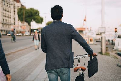 Rear view of man with bicycle on street in city