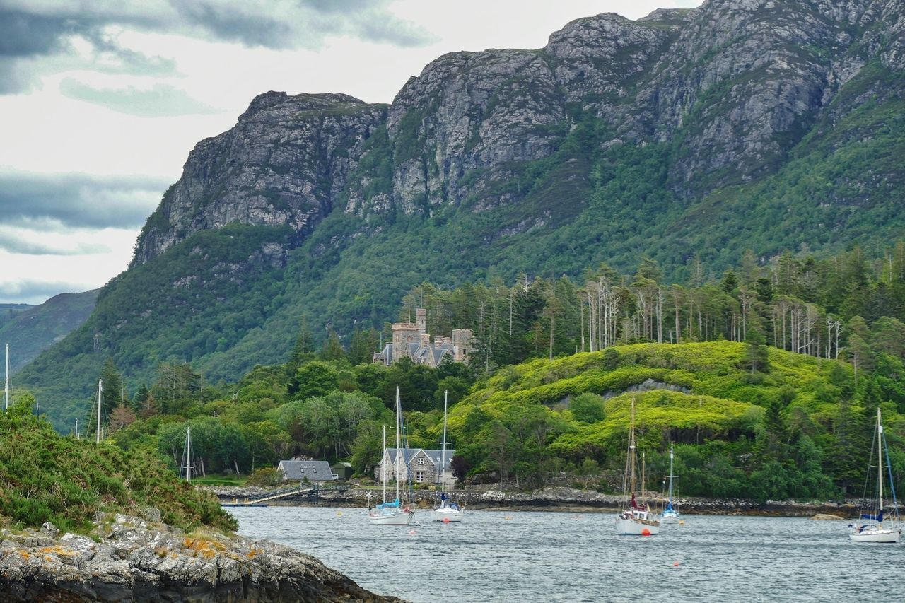 mountain, water, tree, plant, scenics - nature, nautical vessel, beauty in nature, nature, mountain range, day, tranquil scene, tranquility, transportation, waterfront, sky, non-urban scene, green color, rock, mode of transportation, no people, outdoors, sailboat, formation