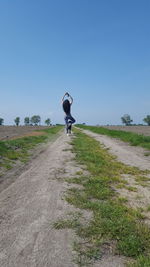 Rear view of woman standing on one leg with arms raised on field