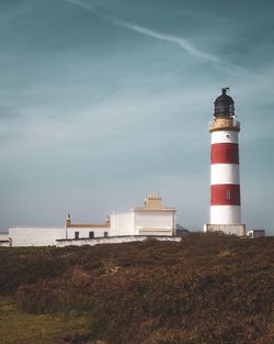 Lighthouse on field by building against sky