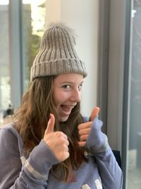 Portrait of smiling young woman wearing hat gesturing thumbs up sign