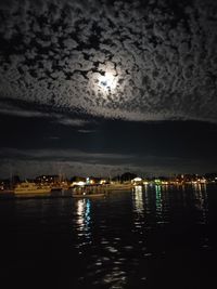 Sea by illuminated city against sky at night