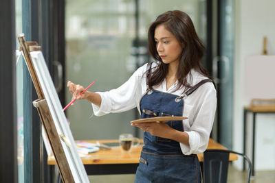 Young woman holding book while standing on shelf