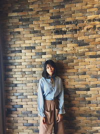 Portrait of young woman standing against brick wall