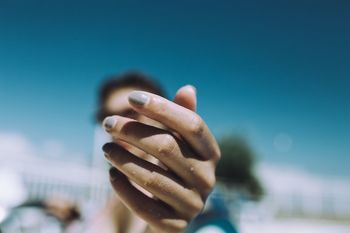 Low angle view of woman with nail polish against clear blue sky