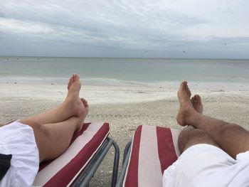 Low section of men sitting on beach against sky