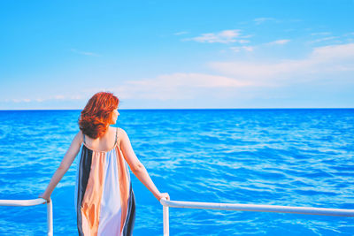 Rear view of woman standing by blue sea against sky