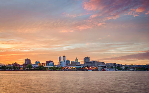 Buildings and river against cloudy sky during sunset