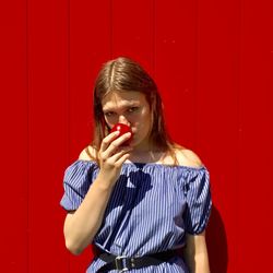 Portrait of young woman standing against red wall