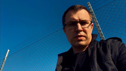 Low angle portrait of man by chainlink fence