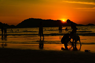 Silhouette people on beach against orange sky