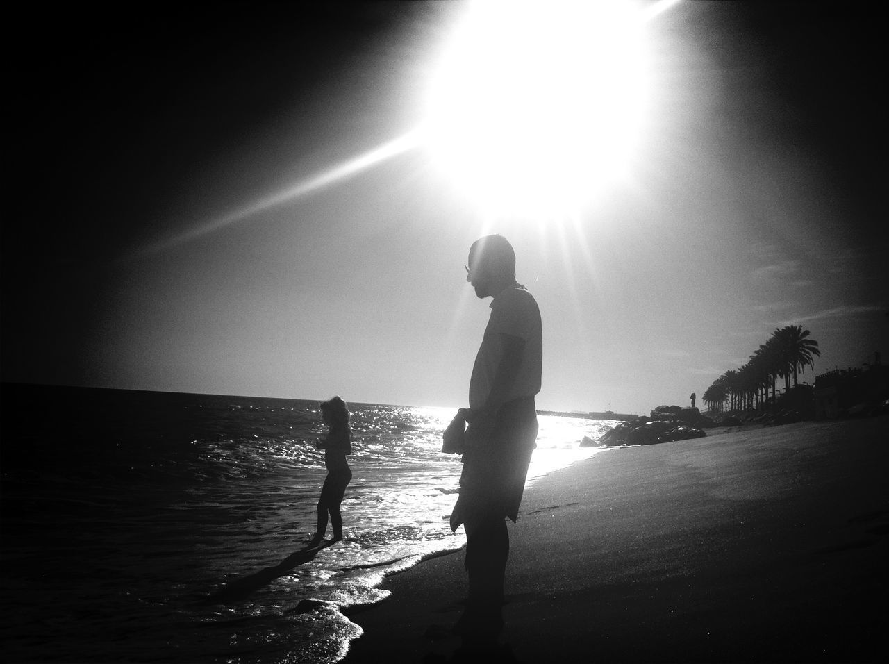 water, sun, sea, lifestyles, leisure activity, silhouette, full length, sunlight, sunbeam, men, standing, horizon over water, lens flare, sky, reflection, boys, rear view, beach