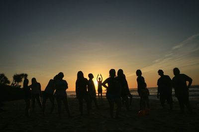 Silhouette people standing on beach against sky during sunset