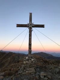 Cross on rock against sky during sunset