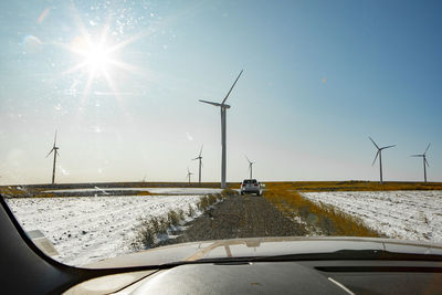 Wind turbines in a field with blue sky through car window