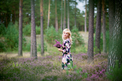 Side view portrait of young woman holding flowers at forest