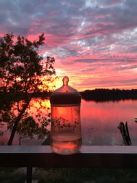 Drink in container on railing against lake and sky during sunset