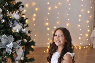 Portrait of young woman standing by christmas tree at home