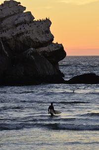 Silhouette man on rock by sea against sky during sunset