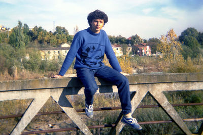 Full length of young man sitting on staircase against sky