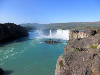 Scenic view of waterfall against clear blue sky