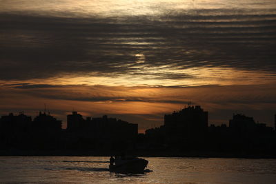 Silhouette cityscape by sea against sky during sunset