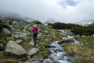 Man standing on rocks by waterfall against sky