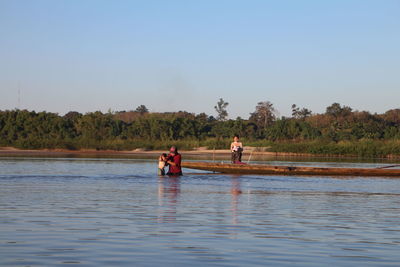 People on lake against clear sky