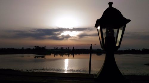 Silhouette street light by lake against sky during sunset