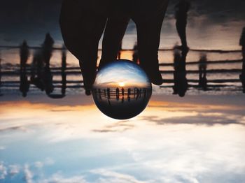 Reflection of silhouette person on crystal ball against sky during sunset