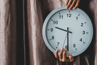 Cropped hands holding clock against curtain