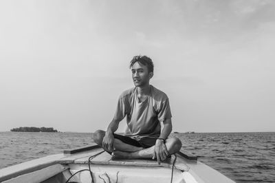 Young man sitting on boat in sea against sky