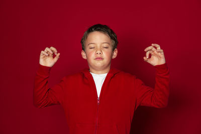 Smiling boy meditating while standing against red background