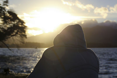 Rear view of woman standing against sea during sunset