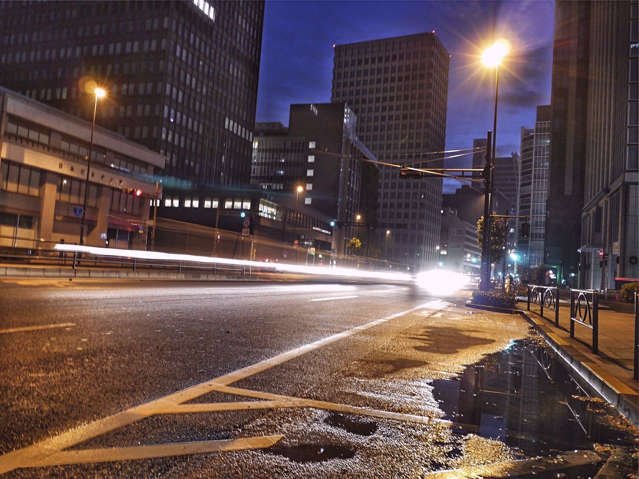 building exterior, architecture, city, built structure, transportation, illuminated, street, road, city street, street light, city life, night, car, skyscraper, office building, land vehicle, modern, building, road marking, mode of transport