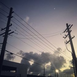 Low angle view of electricity pylon against cloudy sky