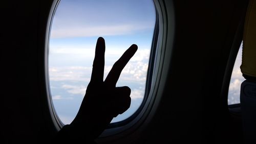 Close-up of silhouette hand against sky seen from airplane window