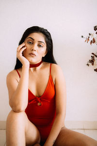 Portrait of young woman sitting against wall at home