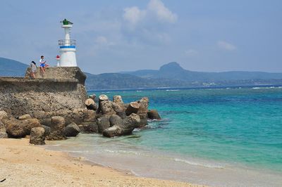 Lighthouse on rocks by sea against sky