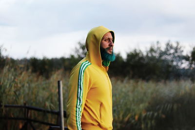 Thoughtful man wearing yellow hooded shirt while standing on field
