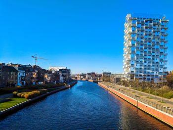 Canal amidst buildings in city against clear blue sky