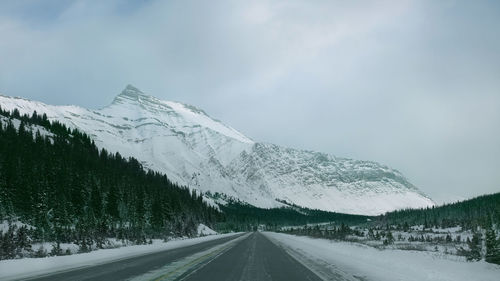 Road by snowcapped mountains against sky