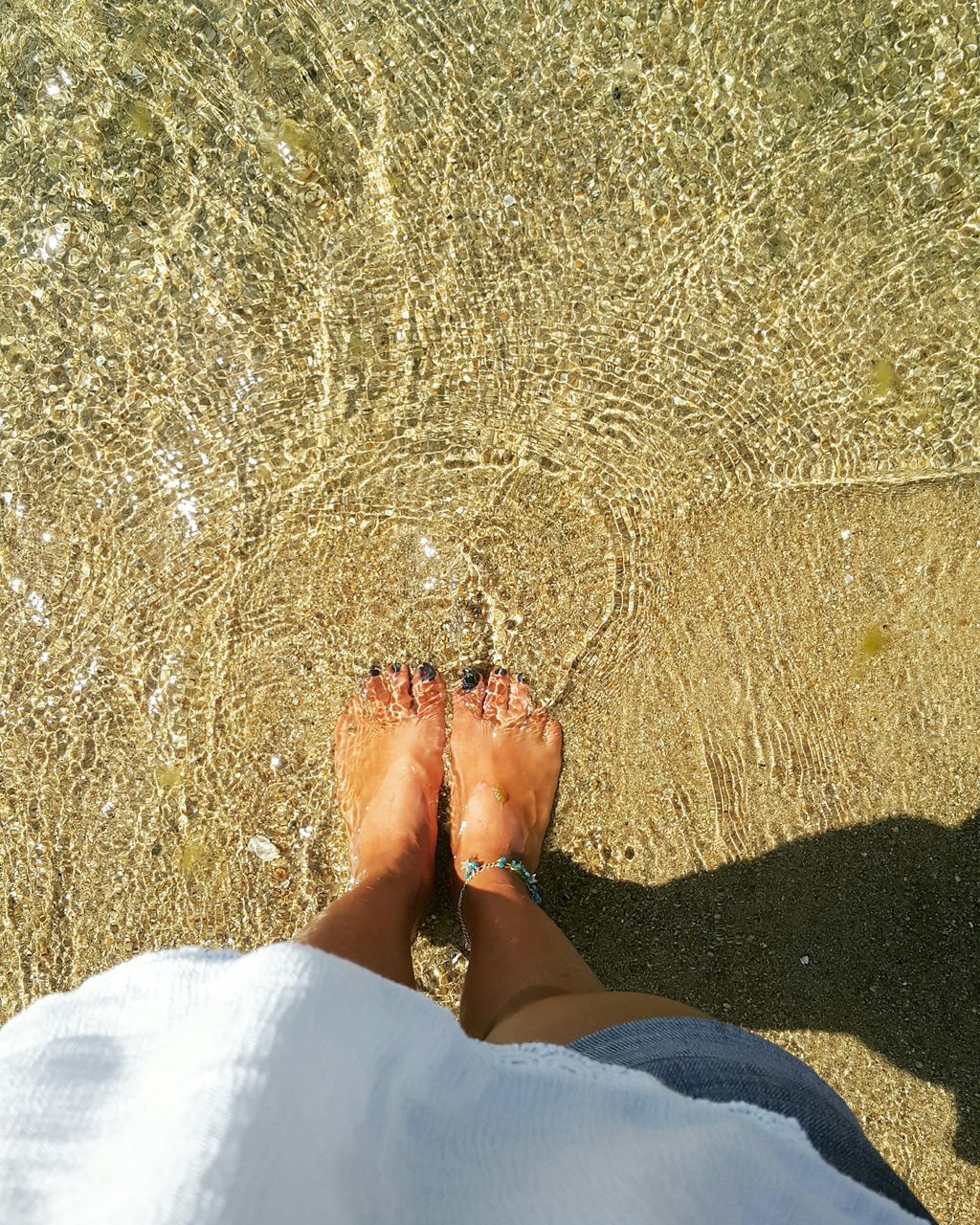 low section, person, beach, water, sand, shore, high angle view, personal perspective, barefoot, sea, lifestyles, leisure activity, human foot, vacations, sunlight, standing, relaxation